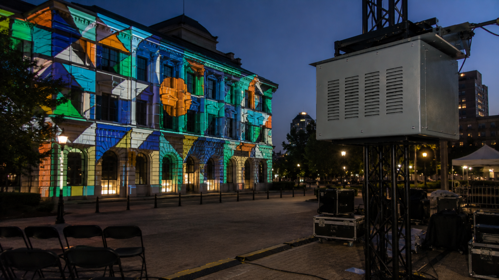 Climate controlled projector enclosure mounted on truss for building projection mapping on an outdoor facade.